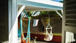 A view through a window of a room with a hammock, a hanging chair, and a small table with a plant. - Villa Gérika, privacy and elegance. Charming villa nestled in a private estate (Sainte-Anne)