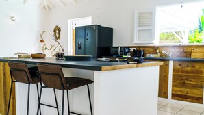A kitchen with a central island, bar stools, a microwave, and a coffee maker. - Villa Gérika, privacy and elegance. Charming villa nestled in a private estate (Sainte-Anne)