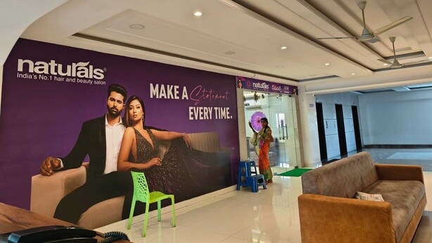 A modern interior with a large advertisement for Naturals, a hair and beauty salon. There is a reception area with a sofa, chairs, and a small table. - Hotel Sri Balaji Inn  (Nirmal)