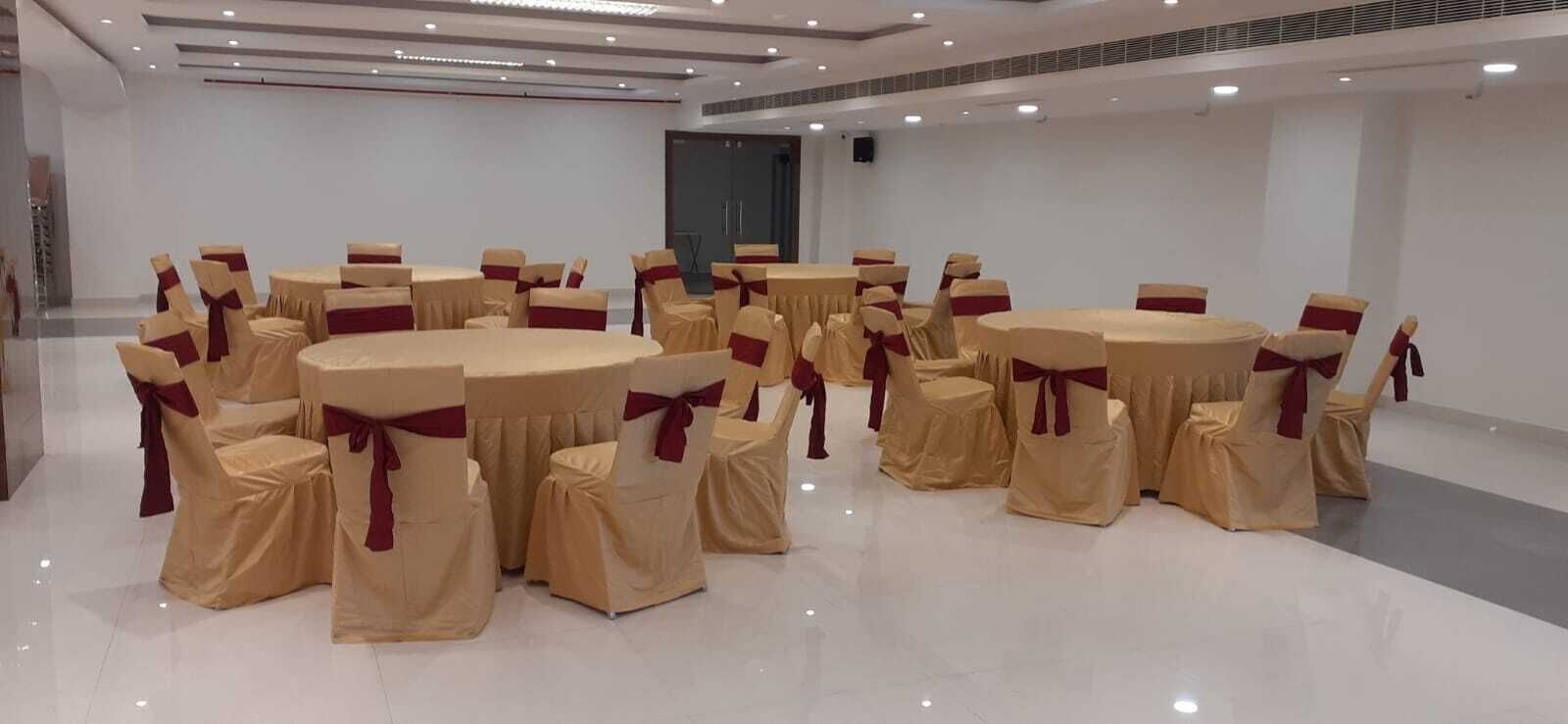 Un salón de conferencias con mesas y sillas redondas, todo cubierto con manteles beige y fajas rojas.