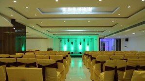 A conference room with rows of chairs, a stage with green lighting, and a chandelier. - Hotel Sri Balaji Inn  (Nirmal)