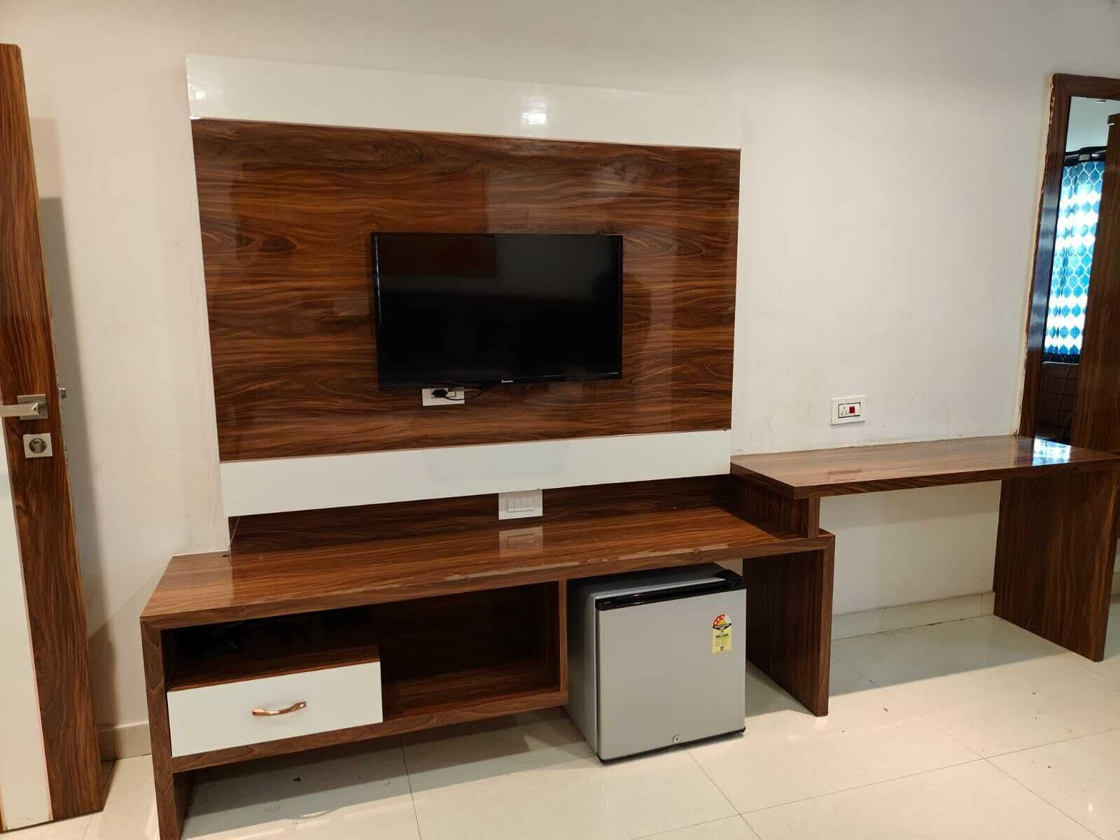A modern living room with a flat-screen TV mounted on a wooden wall unit, a built-in mini-fridge, and a wooden bench.