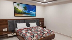 A bedroom with a bed, nightstands, a wall-mounted TV, and a painting of a beach scene. - Hotel Sri Balaji Inn  (Nirmal)