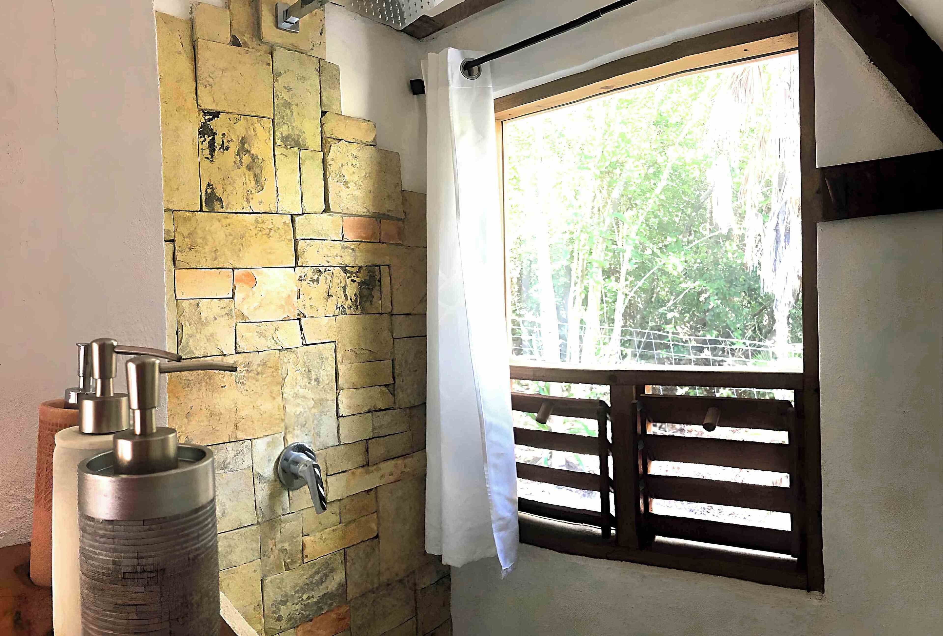 A bathroom with a stone wall, a shower, and a window with a view of trees.