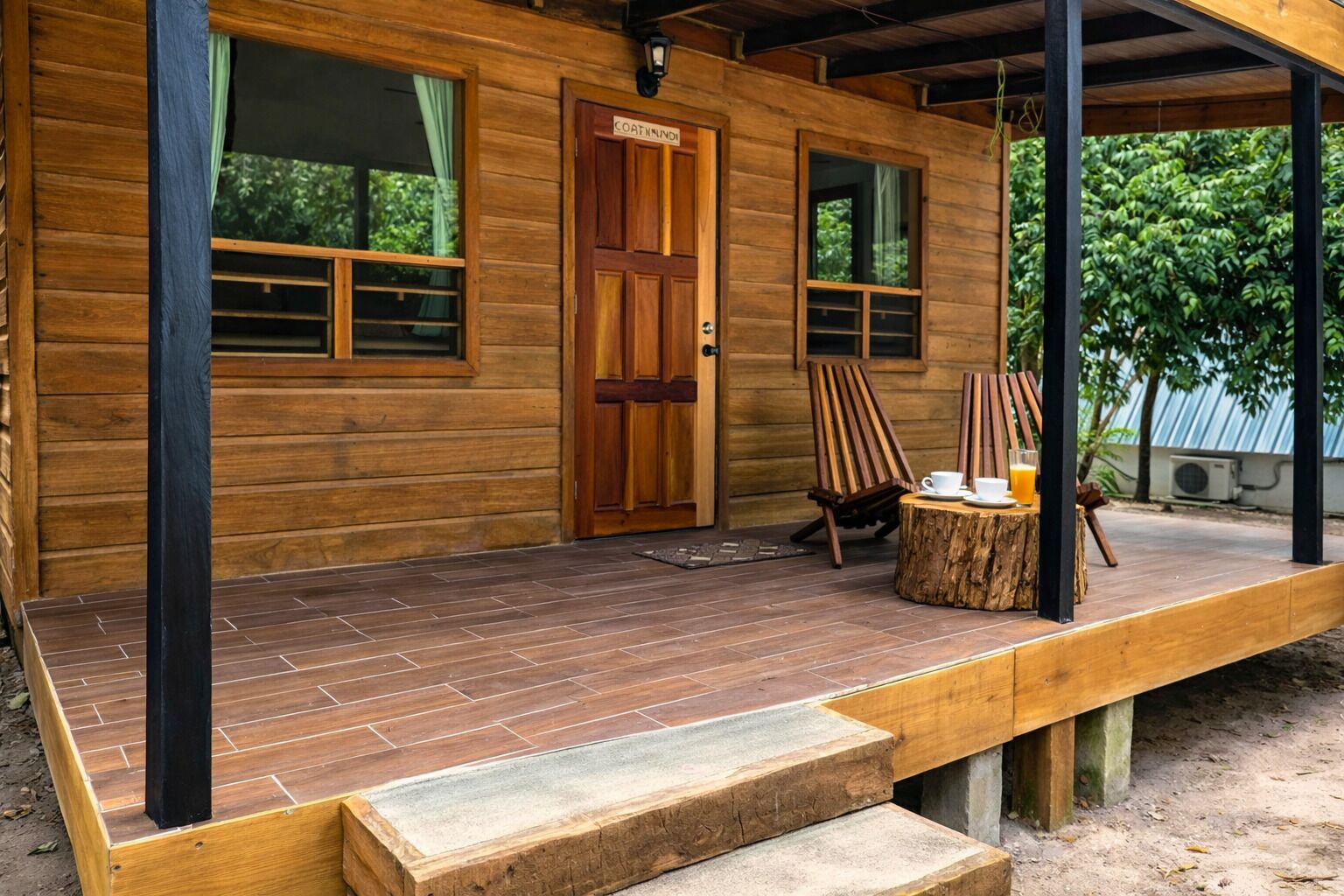 A wooden cabin with a porch, a door labeled 'COATNINGS,' two windows, and a table with chairs outside.