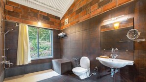 A bathroom with a bathtub, toilet, and sink, featuring dark tiled walls and a window with a view of greenery. - Lazy Hills by Xplore Indo (Kotagiri)