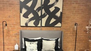 A bed with a grey headboard, black bedding, and white and black pillows. There are two floor lamps on either side of the bed.