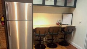 A kitchen with a stainless steel refrigerator, a dining table with four chairs, and a wooden floor.