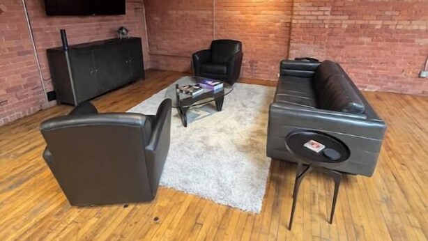 A modern living room with a brick wall, wooden flooring, a flat-screen TV, a sofa, a chair, and a coffee table.