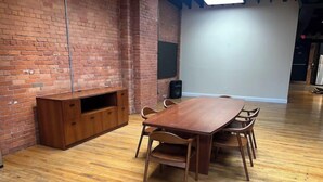 A conference room with a wooden table and chairs, a brick wall, and a whiteboard.