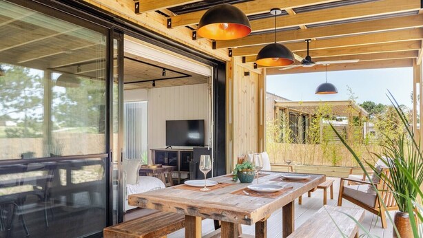 An open-plan living area with a wooden deck, a dining table set for four, and a television mounted on a wall. - Modern House near the Beach (Punta Ballena)