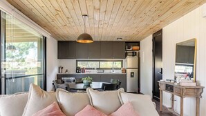 A modern living room with a wooden ceiling, a dining area, and a kitchen with dark cabinets and stainless steel appliances. - Modern House near the Beach (Punta Ballena)