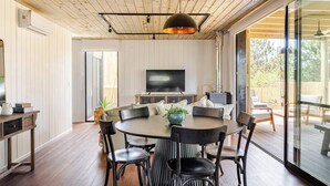A modern living room with a round table, black chairs, a flat-screen TV, and a large window offering a view of the outdoors. - Modern House near the Beach (Punta Ballena)