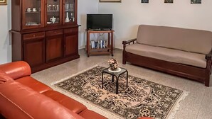 Un salón con un sofá de cuero marrón, un mueble de madera, un televisor sobre un soporte y una alfombra estampada.