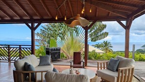 Un espace extérieur abrité, aménagé avec des sièges et offrant une vue sur l’océan, comprenant un barbecue et une table ronde avec des chaises.