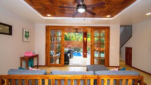 A spacious room with a ceiling fan, a wooden bench, and a view of an outdoor area with a pool and patio furniture. - 3 min walk to surf, 3bedrooms, Villa, Pool, Steps to the Beach! (Uvita)