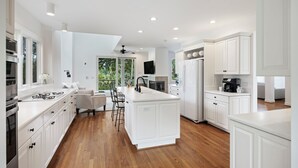 A modern kitchen with white cabinetry, a central island, and a dining area with chairs. - Beautiful Bluebill Home on Kiawah, Private Pool, Pond and Golf Views! (Kiawah Island)