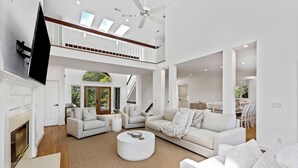 A spacious living room with a high ceiling, a fireplace, and a large window. - Beautiful Bluebill Home on Kiawah, Private Pool, Pond and Golf Views! (Kiawah Island)