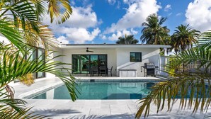 A modern house with a swimming pool, surrounded by palm trees and a clear blue sky.
