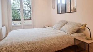 Un dormitorio con cama, lámpara de noche, reloj y ventana con vista a vegetación.