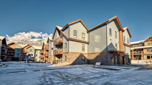 A residential building with a stone facade, multiple balconies, and a clear view of snow-covered mountains in the background.