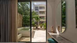 Una habitación de hotel moderna con un puertas corredera de vidrio que da a un área exterior con piscina y vegetación.