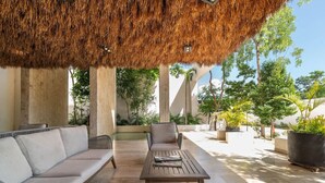 Un área de estar al aire libre con techo de paja, sofás acolchados y una mesa de madera.