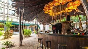 Un área de bar interior con techo de paja, mostrador de bar de madera y taburetes.
