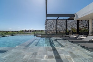 A modern infinity pool with clear water, surrounded by stone tiles and lounge chairs.