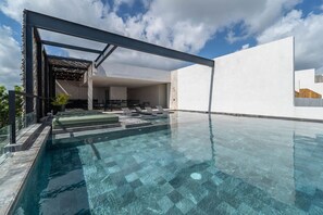 Una piscina exterior moderna amb aigua cristal·lina, envoltada d'una estructura blanca minimalista i una pèrgola.