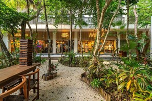 A courtyard with a wooden bench, a stack of wooden blocks, and various plants. - Lux 1BR w/ Rooftop Pool, Close to Beach (Tulum)