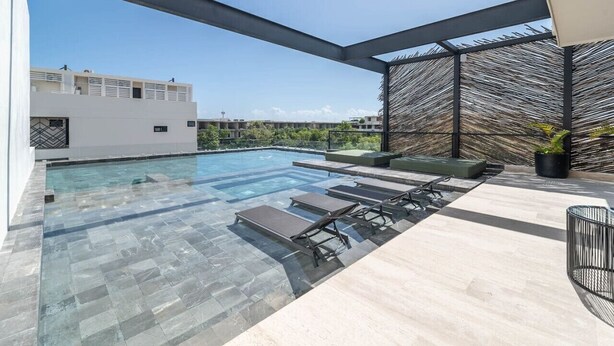A rooftop infinity pool with clear glass edges, surrounded by lounge chairs and a modern outdoor seating area. - Lux 1BR w/ Rooftop Pool, Close to Beach (Tulum)