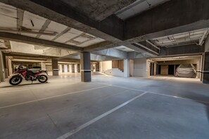 A spacious underground parking area with concrete pillars, a motorcycle, and a covered vehicle.