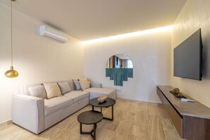 Un saló modern amb un sofà, dues taules petites, un televisió pantalla plana i un aparell d'aire condicionat.