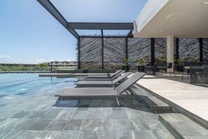 A rooftop infinity pool with lounge chairs, a pergola, and a view of the city skyline. - Lux 1BR w/ Rooftop Pool, Close to Beach (Tulum)