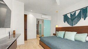 A modern bedroom with a bed, bedside table, and a wall-mounted TV. - Lux 1BR w/ Rooftop Pool, Close to Beach (Tulum)