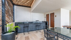 A modern kitchen with a glass island, black bar stools, and a dining table with chairs. - Lux 1BR w/ Rooftop Pool, Close to Beach (Tulum)