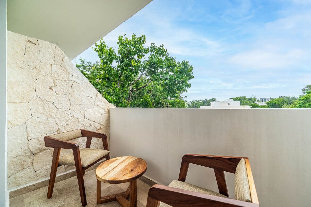 Un balcon avec deux chaises en bois et une petite table ronde, donnant sur un paysage verdoyant et des bâtiments.