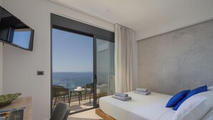 Une chambre moderne avec un grand lit, un téléviseur fixé au mur, un balcon avec vue sur la mer et une petite table avec une chaise.