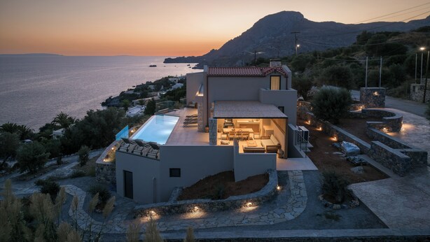 Une maison moderne dotée d’une piscine, d’un chemin en pierre et offrant une vue sur la mer au coucher du soleil.