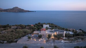 Une propriété située sur la côte, offrant une vue sur la mer, avec une allée pavée, un petit jardin et un bâtiment doté d’une façade en pierre.