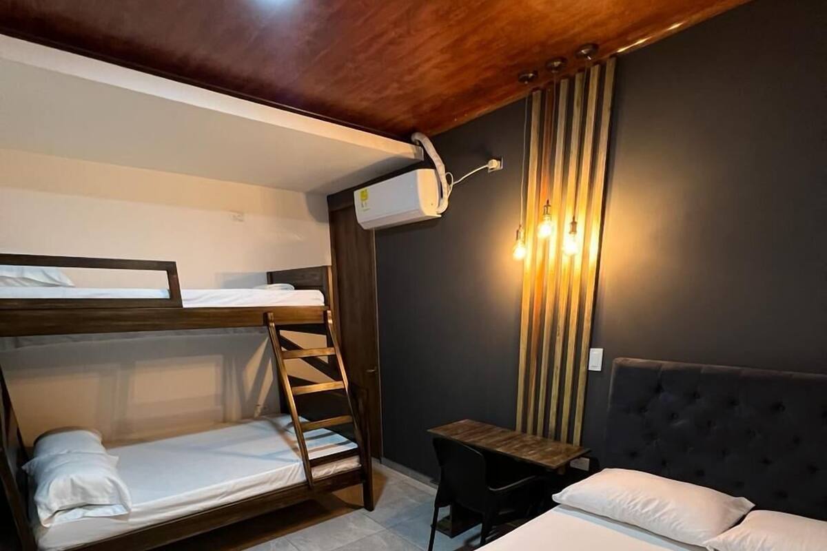 A room with bunk beds, a single bed, a small table, and a wall-mounted light fixture.