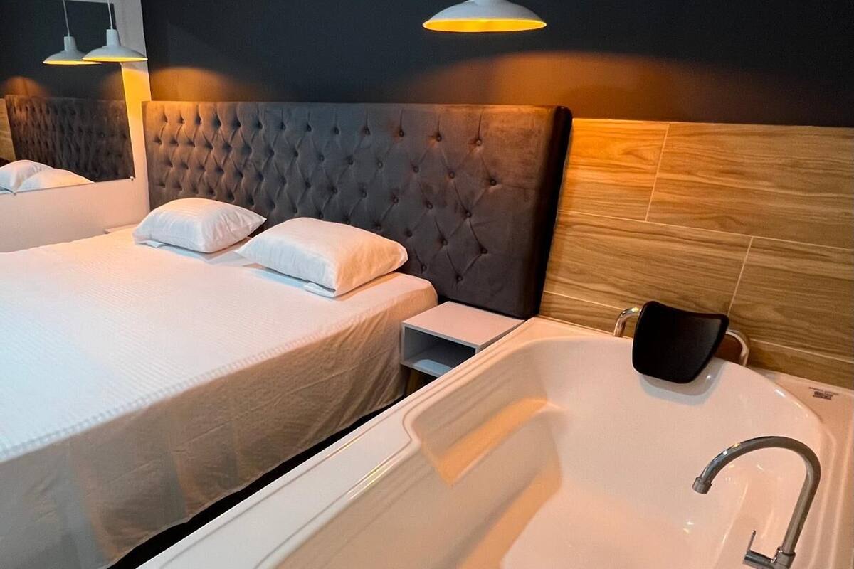 A hotel room with two beds, a large bathtub, and pendant lighting.