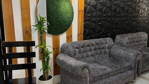 Un salon avec un canapé gris, un miroir rond, une plante en pot et une chaise noire.