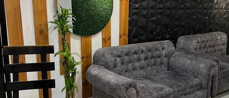 A living room with a grey sofa, a round mirror, a potted plant, and a black chair.