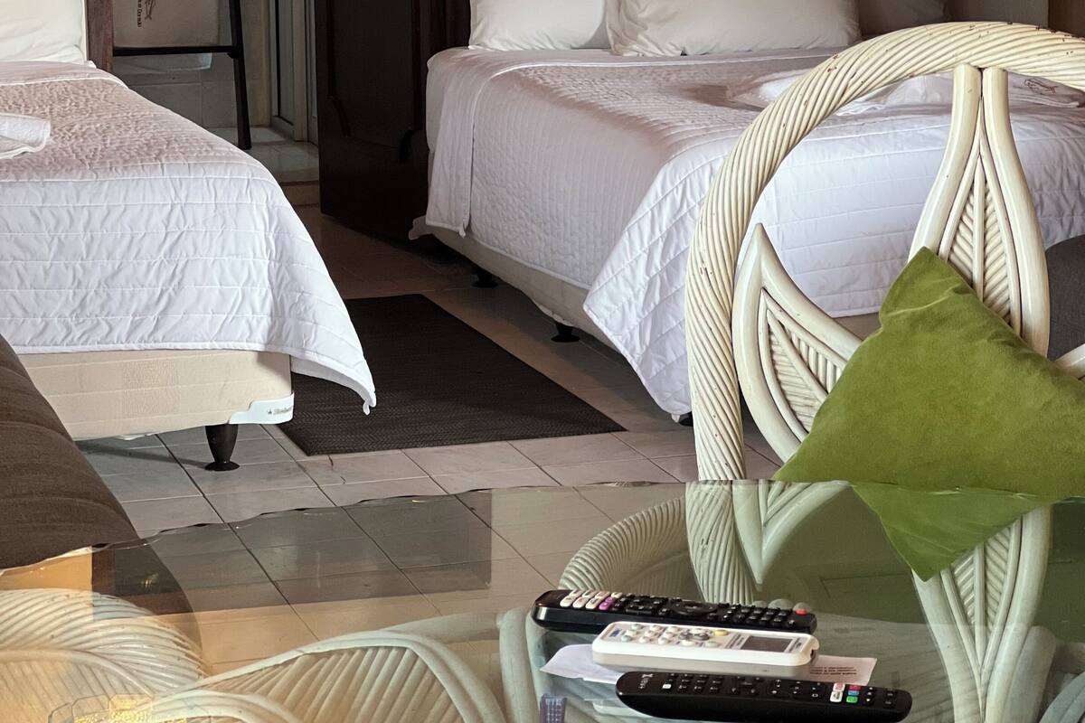 A hotel room with two beds, a wicker chair, and a glass table with remote controls.