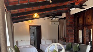 A hotel room with a brick ceiling, white wicker furniture, and two beds with white bedding.