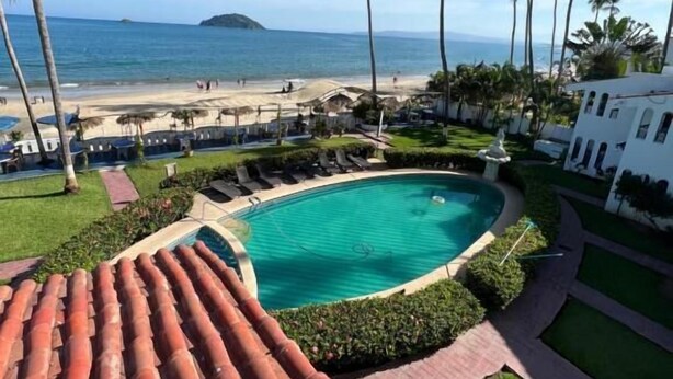 A resort with a swimming pool, palm trees, and a beach view.