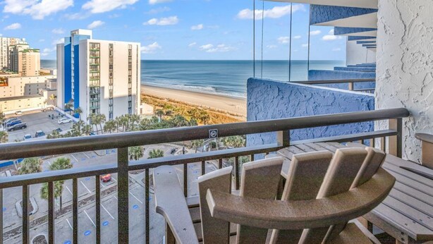 A balcony with a view of the beach and cityscape, featuring a table and chairs. - Bluewater Resort 1012 (Myrtle Beach)