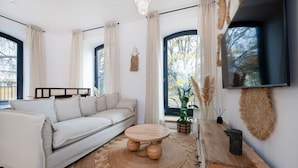 A modern living room with a sofa, a round wooden coffee table, and a TV mounted on the wall. - Łódź Downtown - Parking & Balcony - by Rentujemy (Łódź)